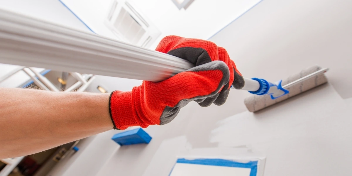 Painter using a roller to apply white paint to an interior wall